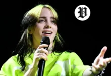 Billie Eilish smiling and holding a microphone while performing live on the 2025 tour