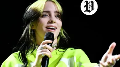 Billie Eilish smiling and holding a microphone while performing live on the 2025 tour