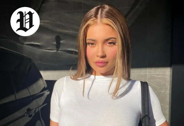 Kylie Jenner posing in natural sunlight wearing a white fitted top.