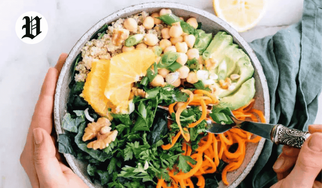 Colorful healthy bowl with fresh vegetables, chickpeas, avocado, orange slices, and greens.