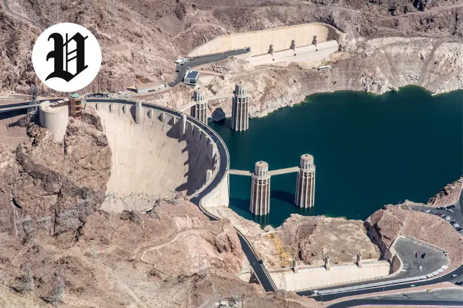 Hoover Dam with Lake Mead reservoir and intake towers surrounded by desert mountains.