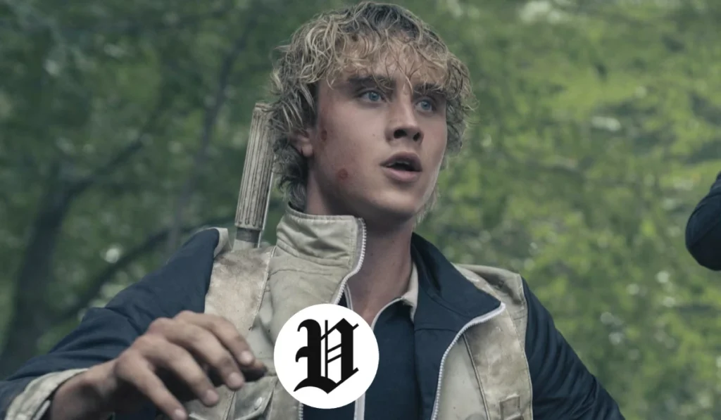Joseph Zada outdoors with wet blond curls, wearing a tactical-style vest and looking surprised in a forest setting.